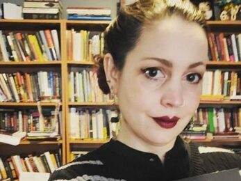 Jeana Jorgenson woman, brown hair pulled off face, red lipstick, dark top in front of bookshelves