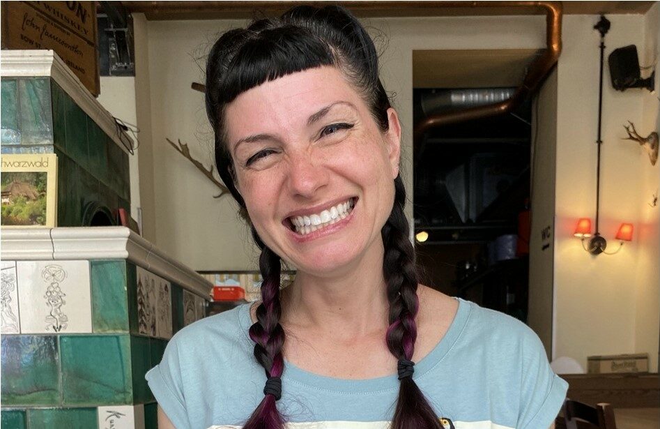 female with brown hair, bangs and 2 braids smiling