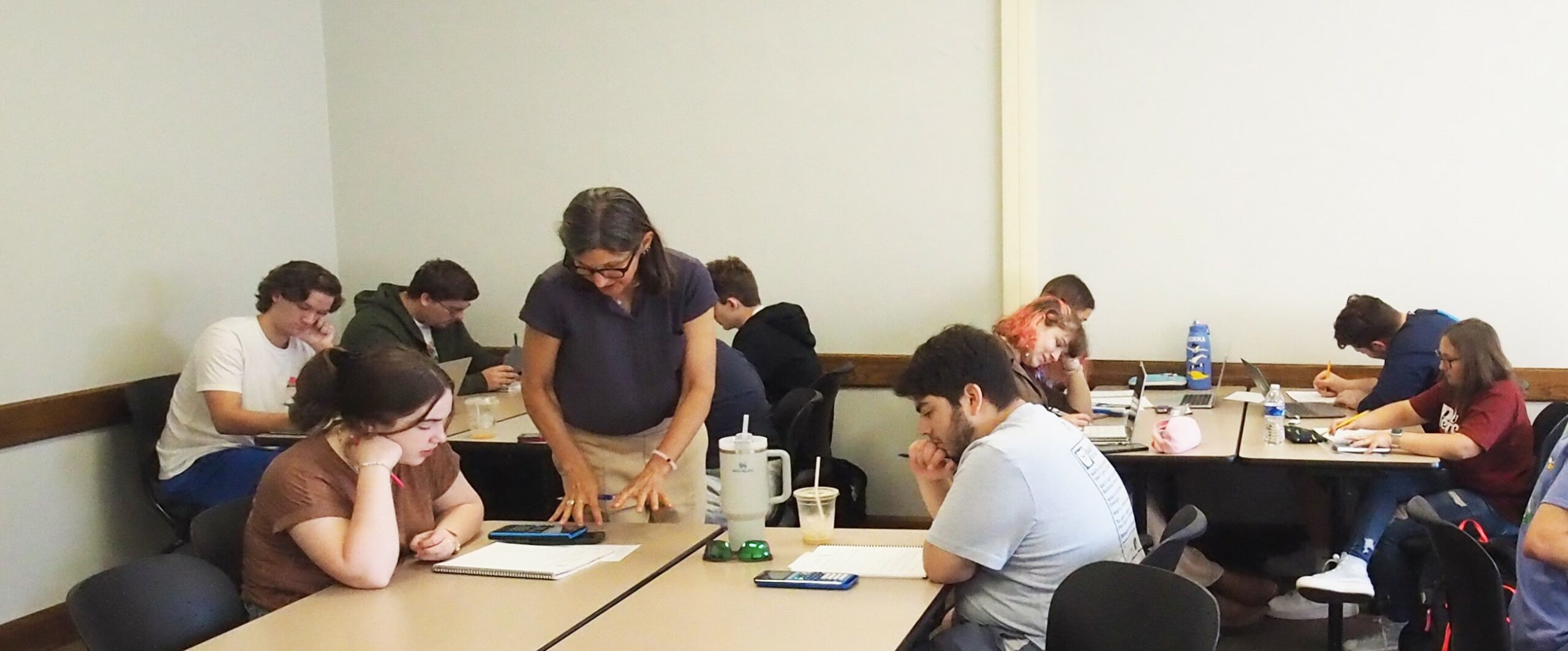 Classroom setting with students at tables and an instructor assisting a student
