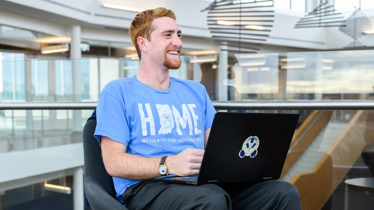 A male student sits on his laptop smiling