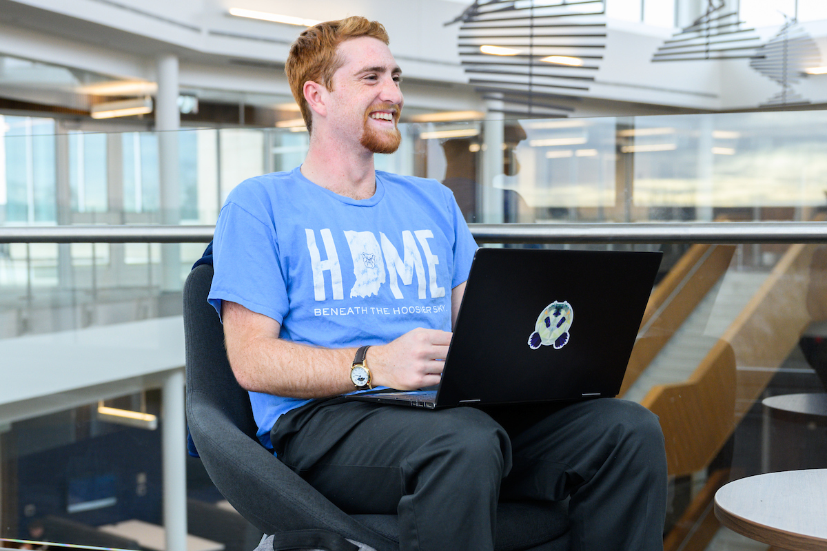 A male student works on his laptop while smiling