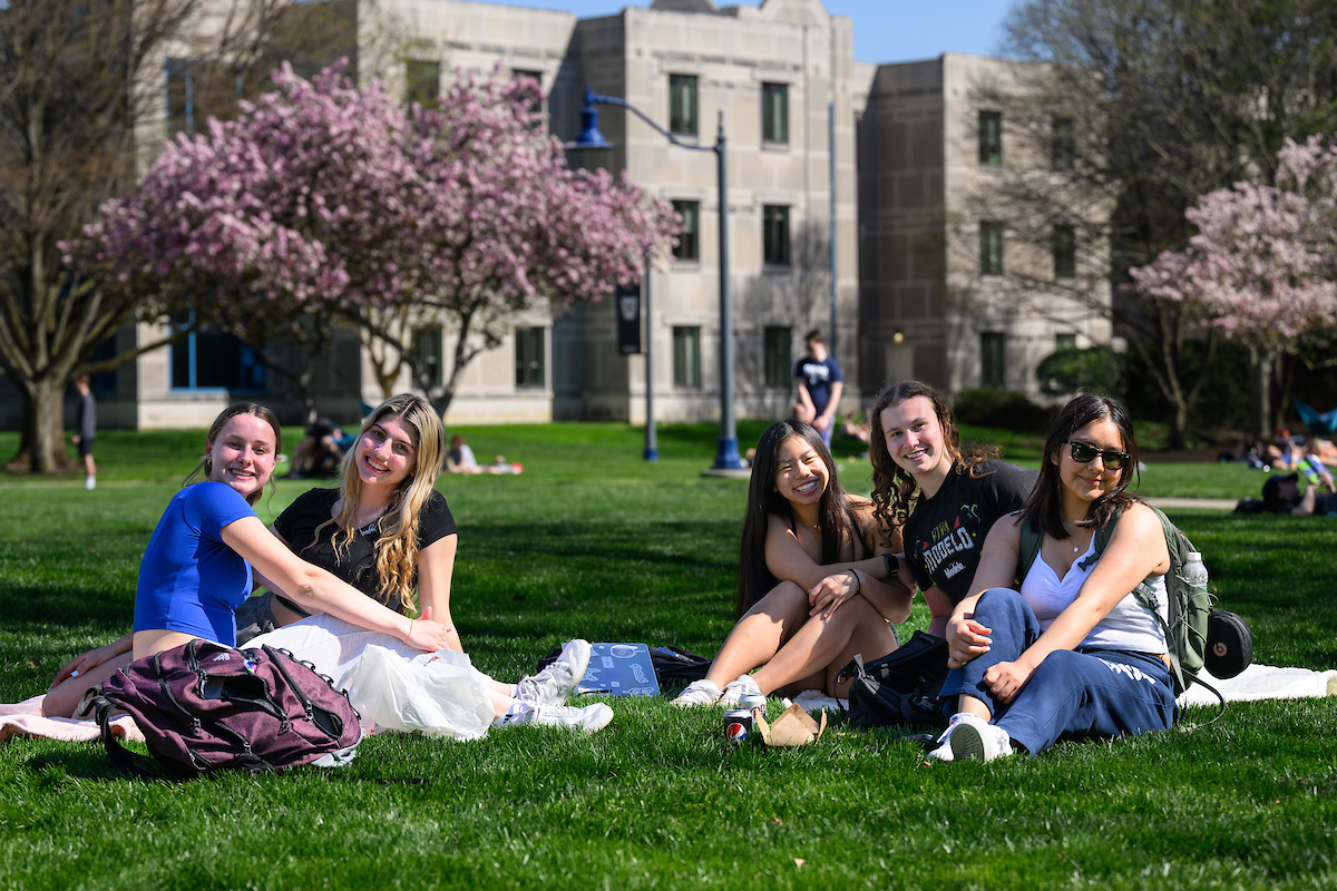 A group of students sits outdoors on grass, smiling.