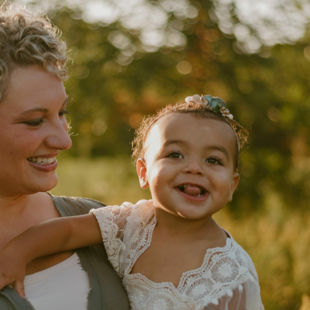 woman with blonde curly hair in gray and white shirt holding toddler girl in white shirt