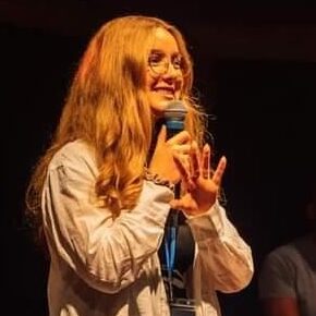 blond woman in beige top standing with microphone