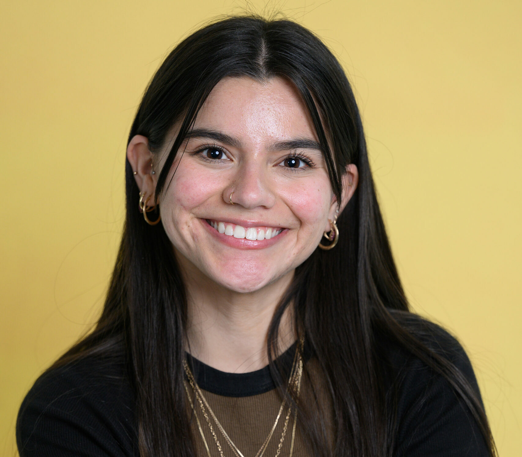 A female student is smiling in front of a yellow background