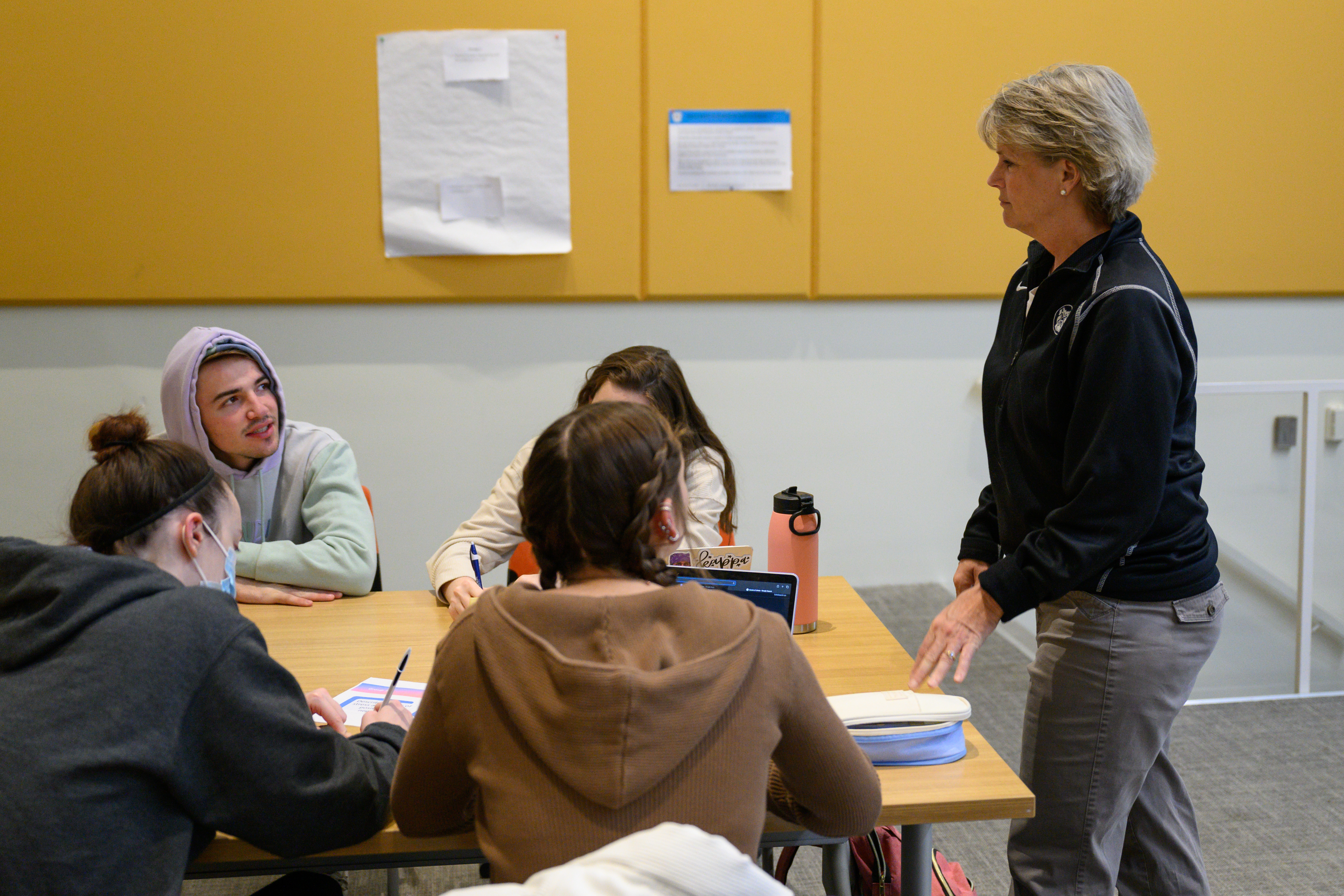 A professor stands at a table talking to a group of four students.