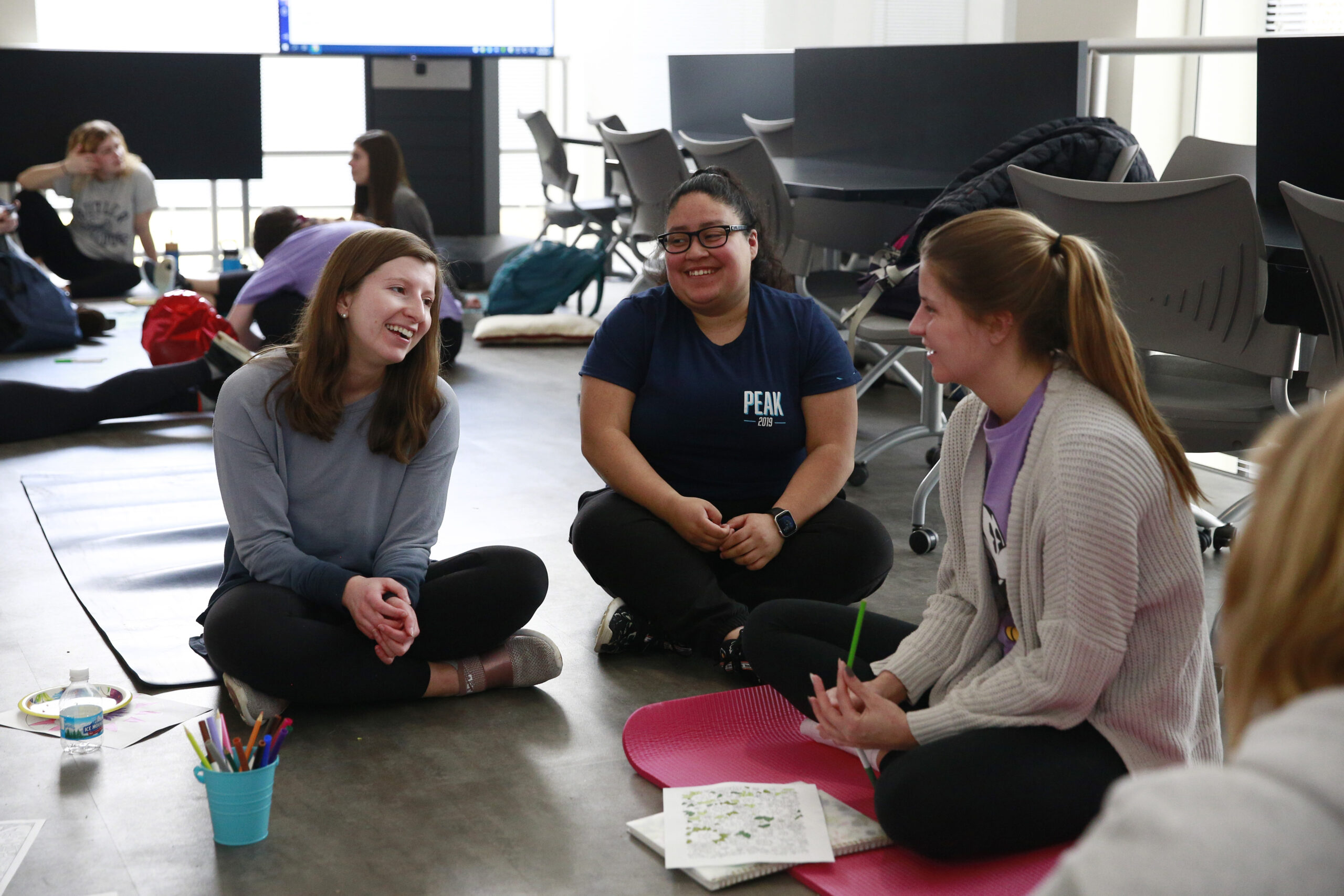 Three female student sit in a circle on the floor and are working on a project.