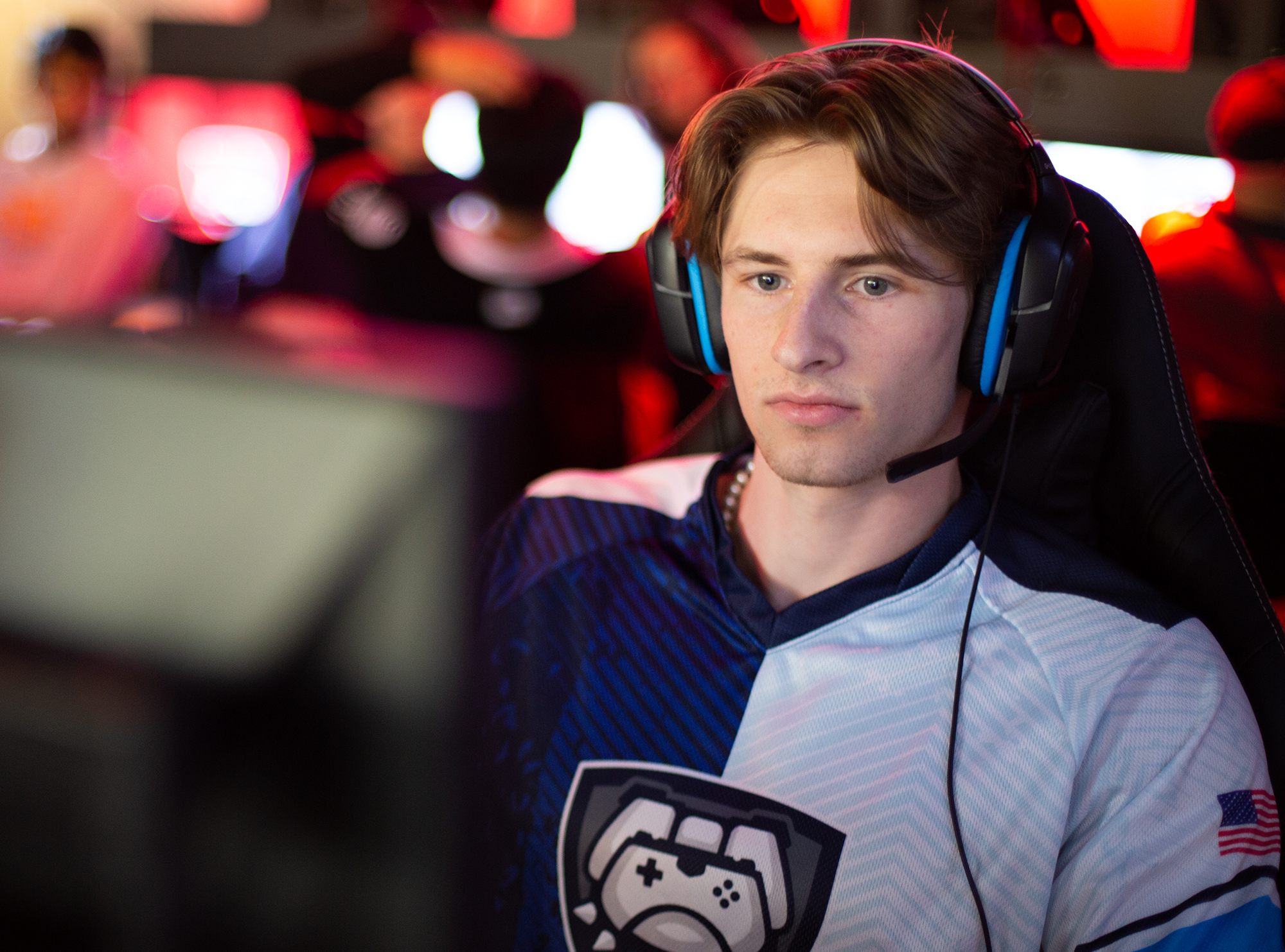 male with brown hair in Butler Esports blue and white jersey wearing headphones with a microphone sitting in front of a computer