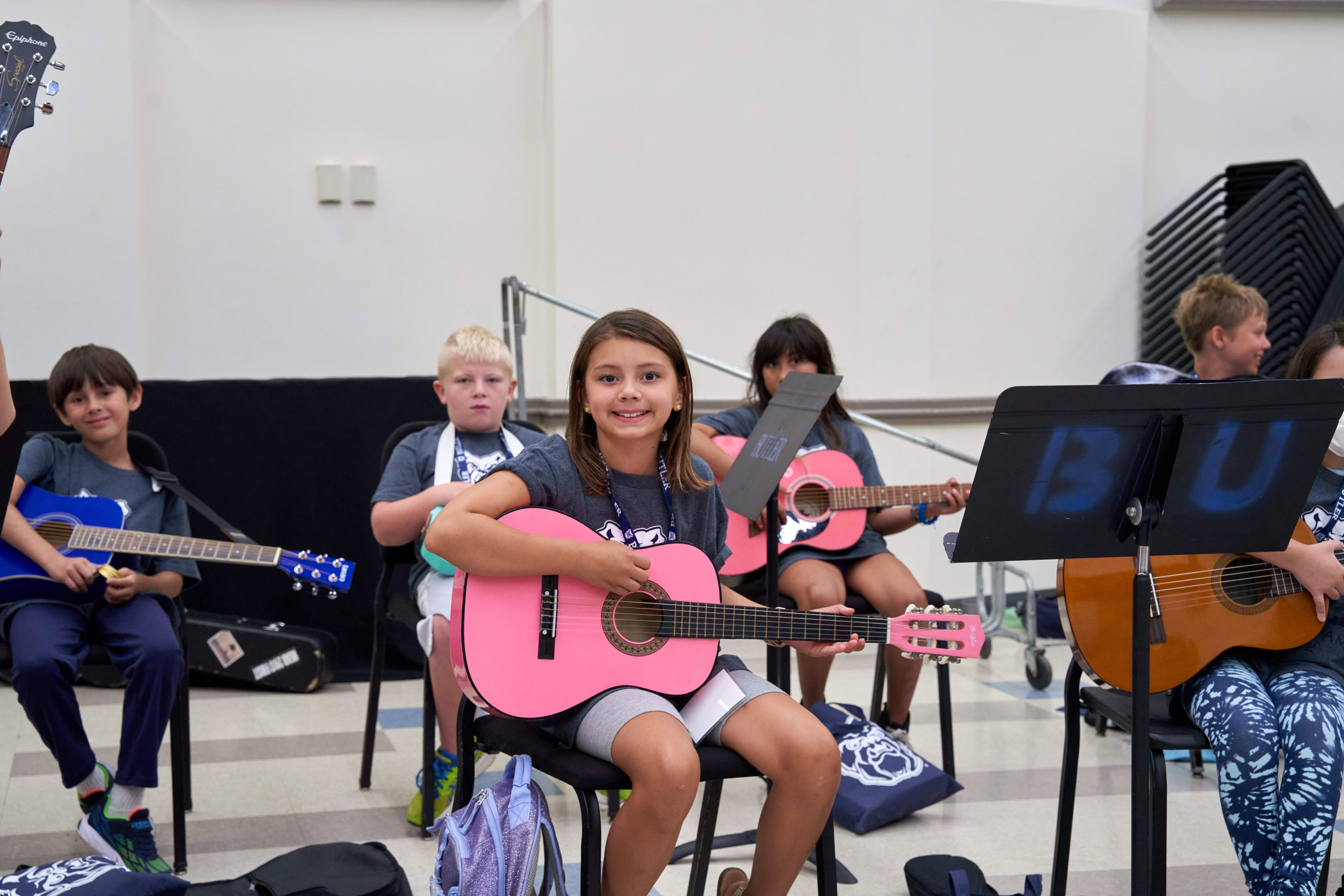 A class of elementary-aged BCAS students learning guitar. One student in the foreground is smiling at the camera