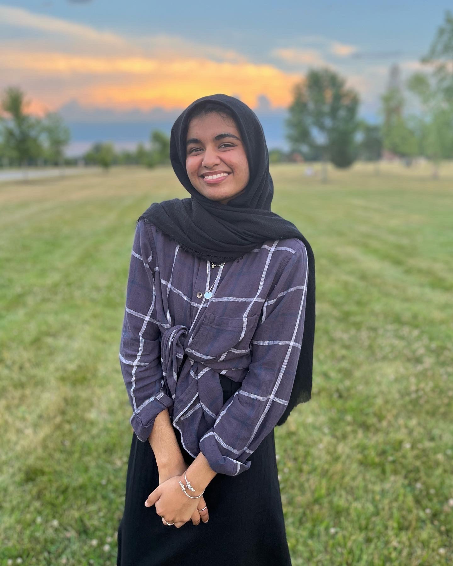 A female student stands outside in a field smiling