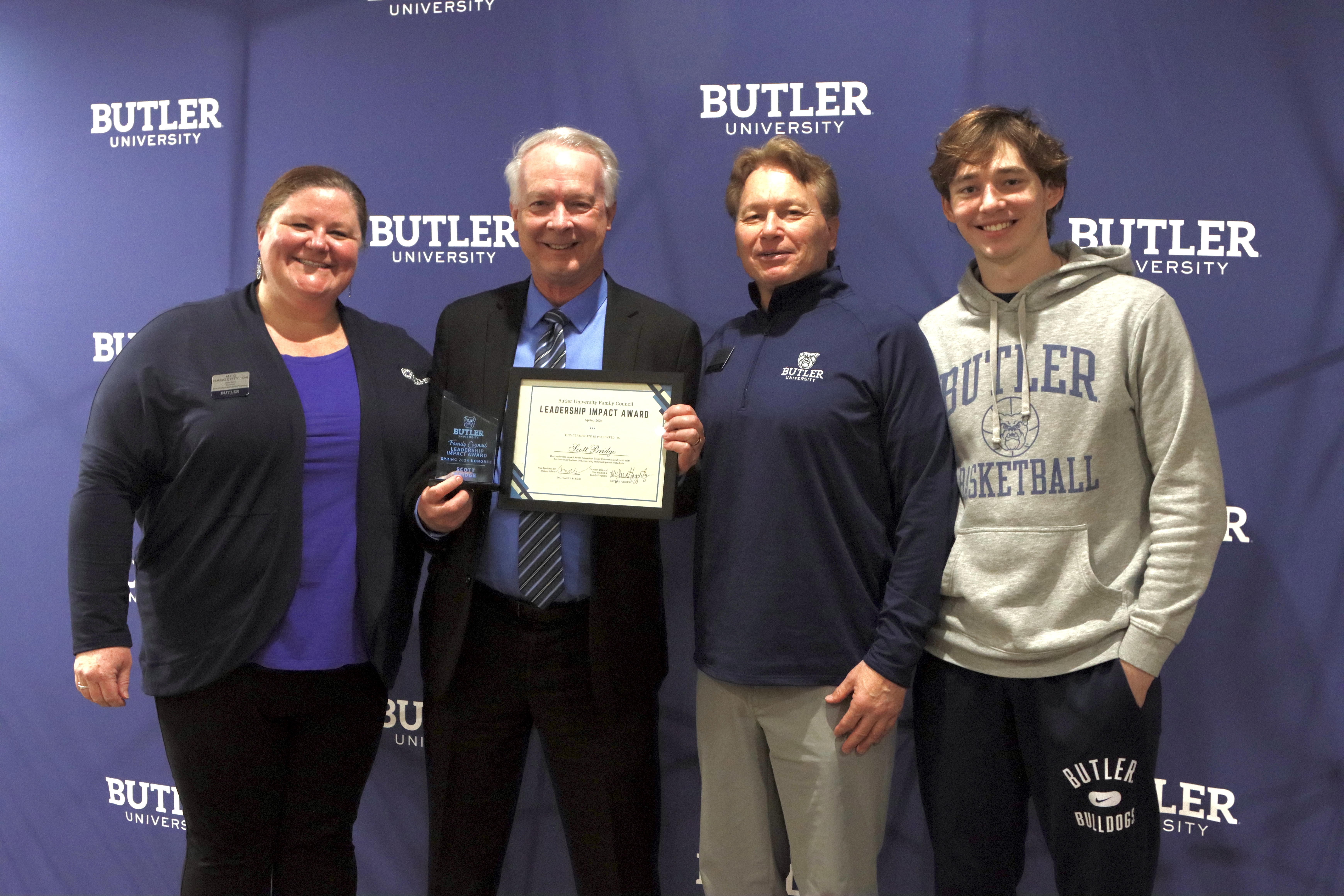 Professor Scott Bridges poses with his certificate and trophy alongside Director of New Student & Family Programs Meg Haggerty (left) and nominating family Glen Danahey and student Brock Danahey (right). Butler University backdrop with four people posing in front. Scott Bridge holding his certificate and trophy.