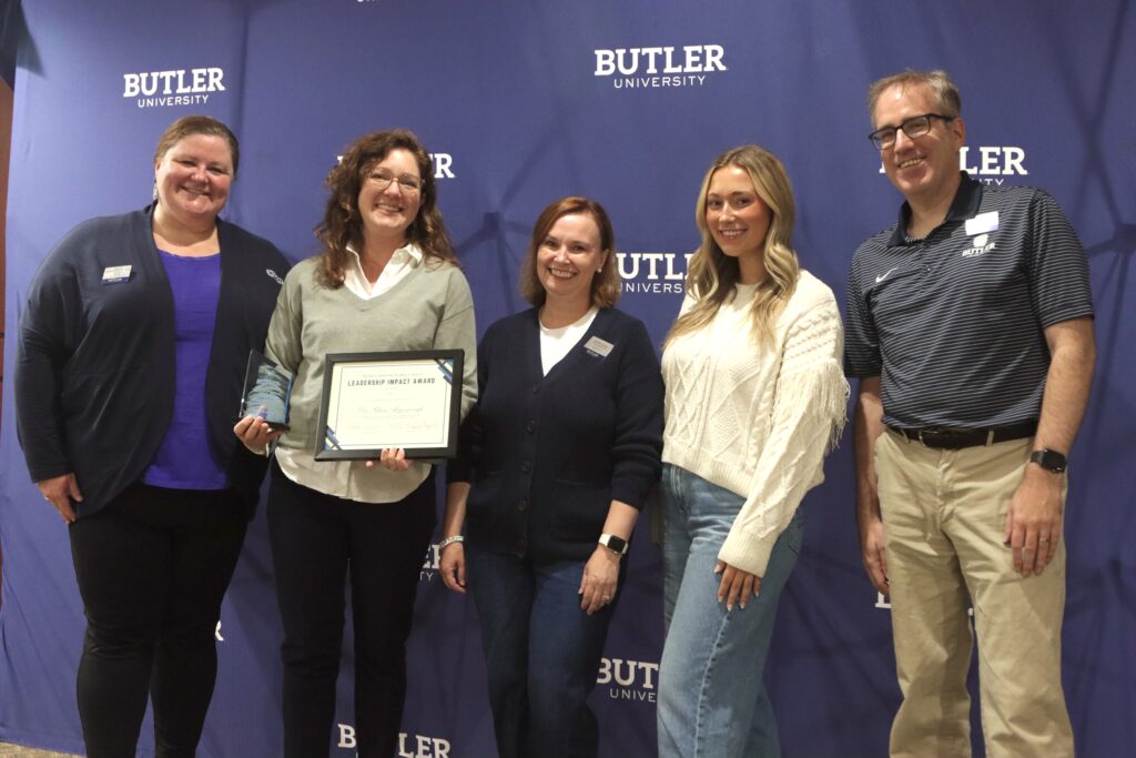 Dr. Rhea Myerscough poses with her certificate and trophy alongside Director of New Student & Family Programs Meg Haggerty (left) and nominating family Shannan & Eric Younger with student Megan McFadden (right). Butler University backdrop with five people posing in front. Dr. Myerscough holding her certificate and trophy.