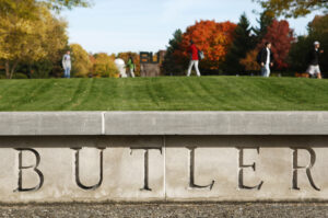 The Butler Lawn; the Butler sign is close and in focus in the foreground, while students walk on the lawn in the background