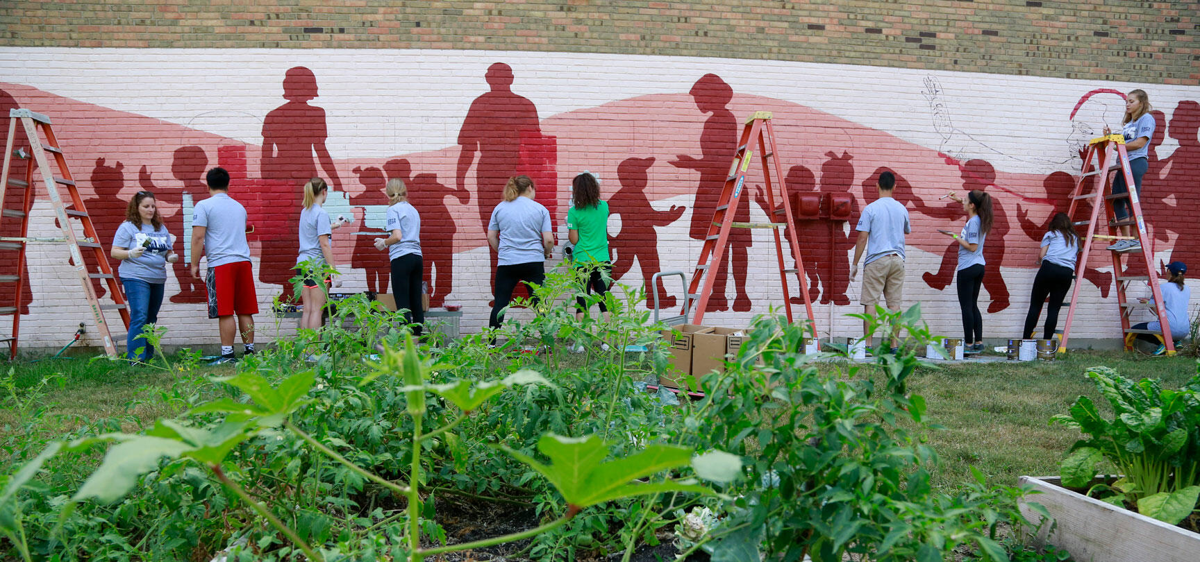 Students paint mural on wall in garden