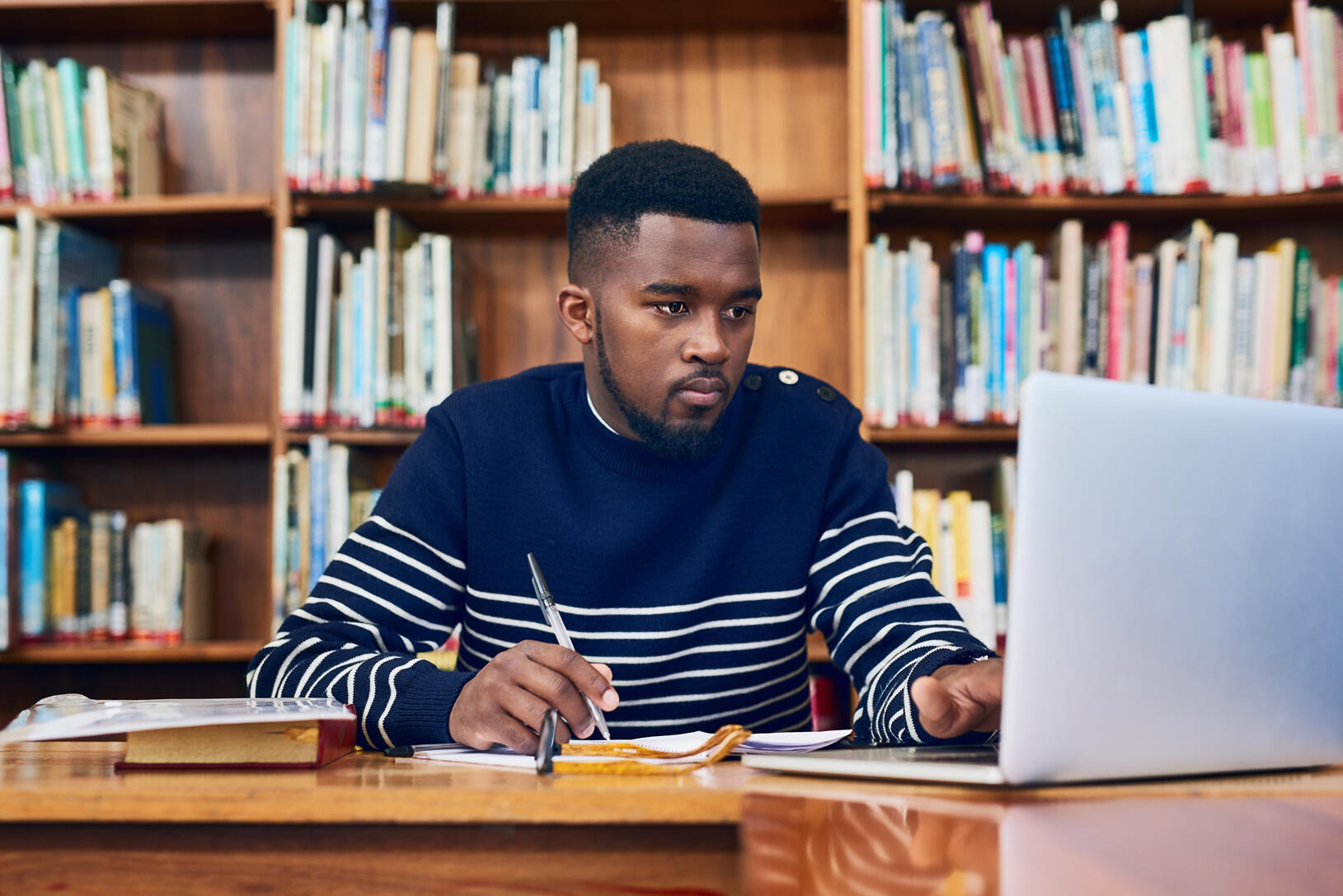 male student in blue and white striped sweater at computer, bookshelves behind