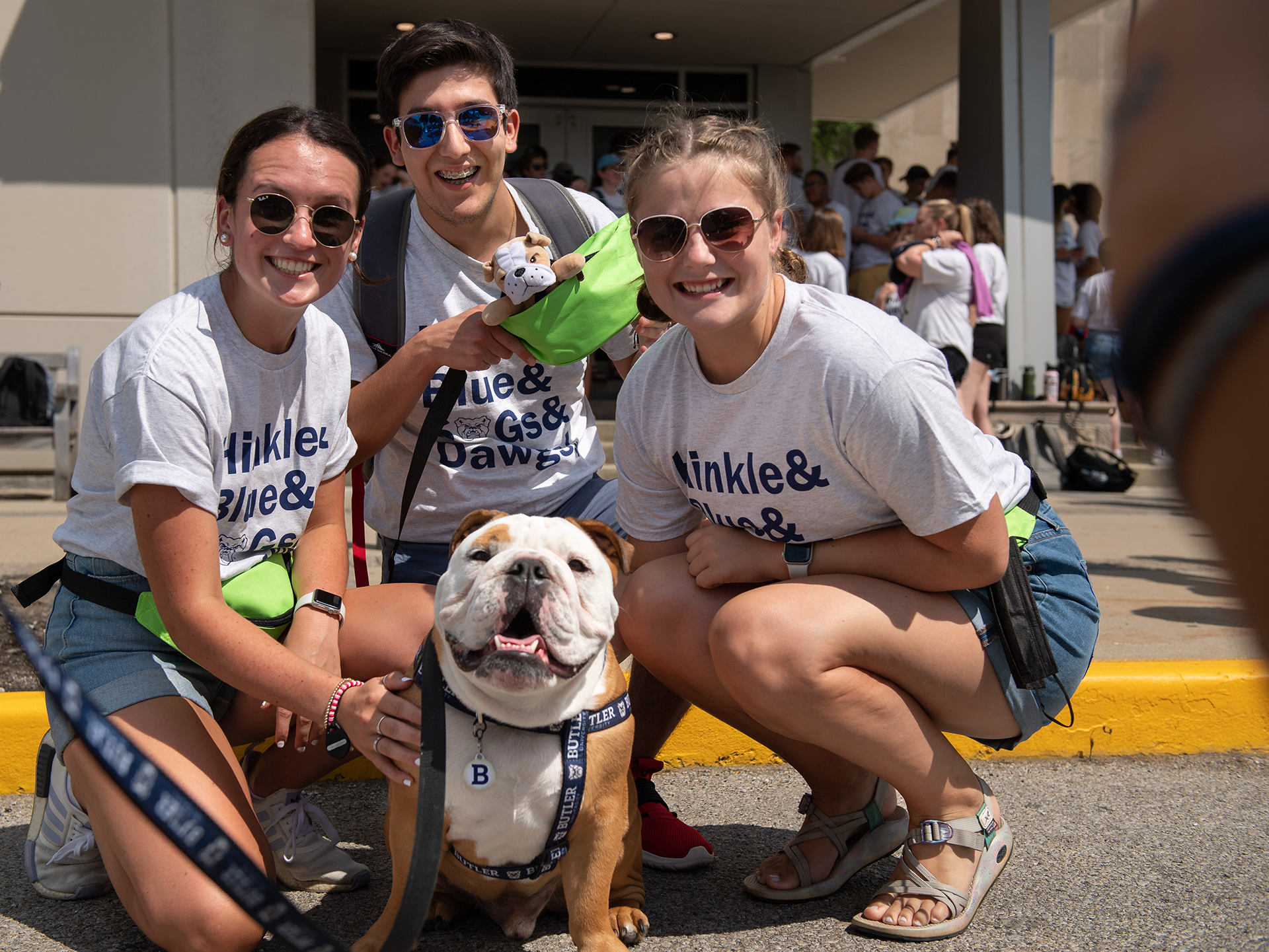 Bulldog in a Butler harness and leash with 3 students around him in white t-shirts and sunglasses