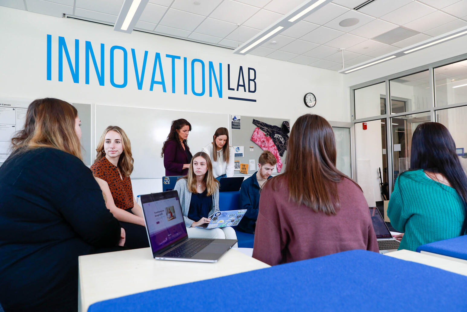 male and female students sitting on blue and white seats. Innovation Lab printed on the white wall
