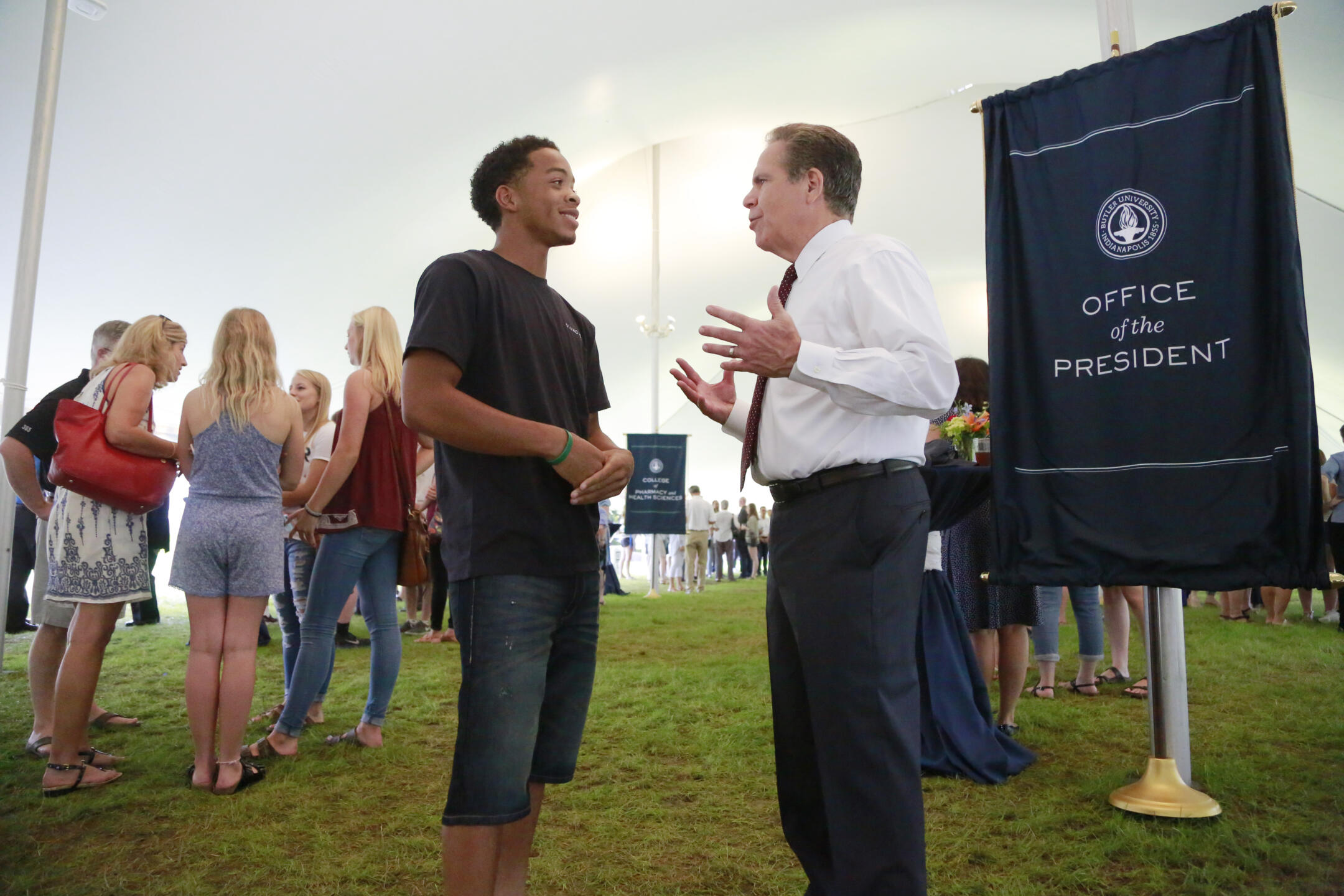president danko in white shirt, red tie, dark pants talking to male student in denim shorts and black t-shirt. signage reads Office of the President