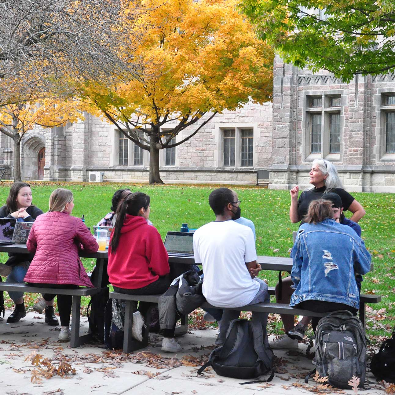 students outside on picnic table being taught by woman with grey hair