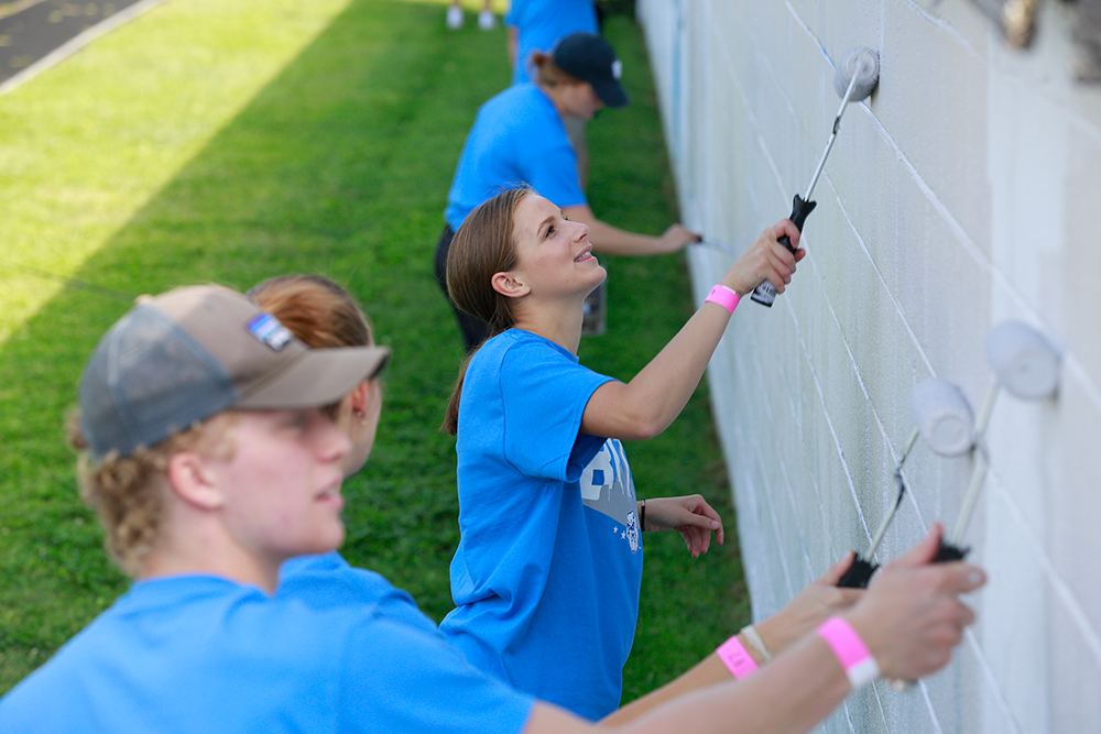 male and female students in blue t-shirts painting a wall