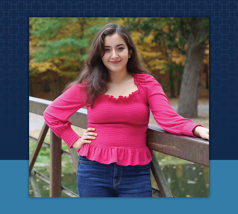 female with brown hair in bright pink shirt and blue jeans standing near fence