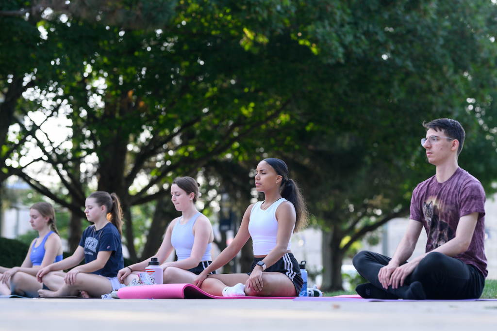 Butler male and female students seated in yoga pose on mats outside