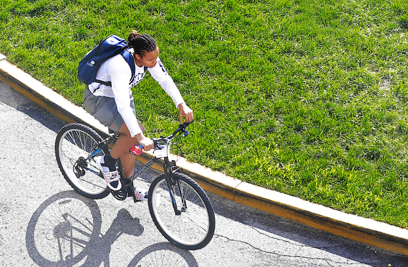 Black male in white shirt with blue backpack on bicycle